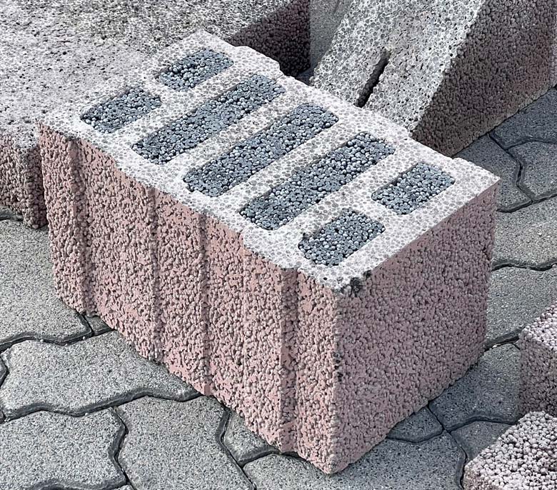 Wandaufbau bei BRALE: Ein rot-lila farbiger Liaplan Ultra 08 Ziegel liegt auf gepflastertem Boden. Der Ziegel ist mit einer grauen Masse gefüllt