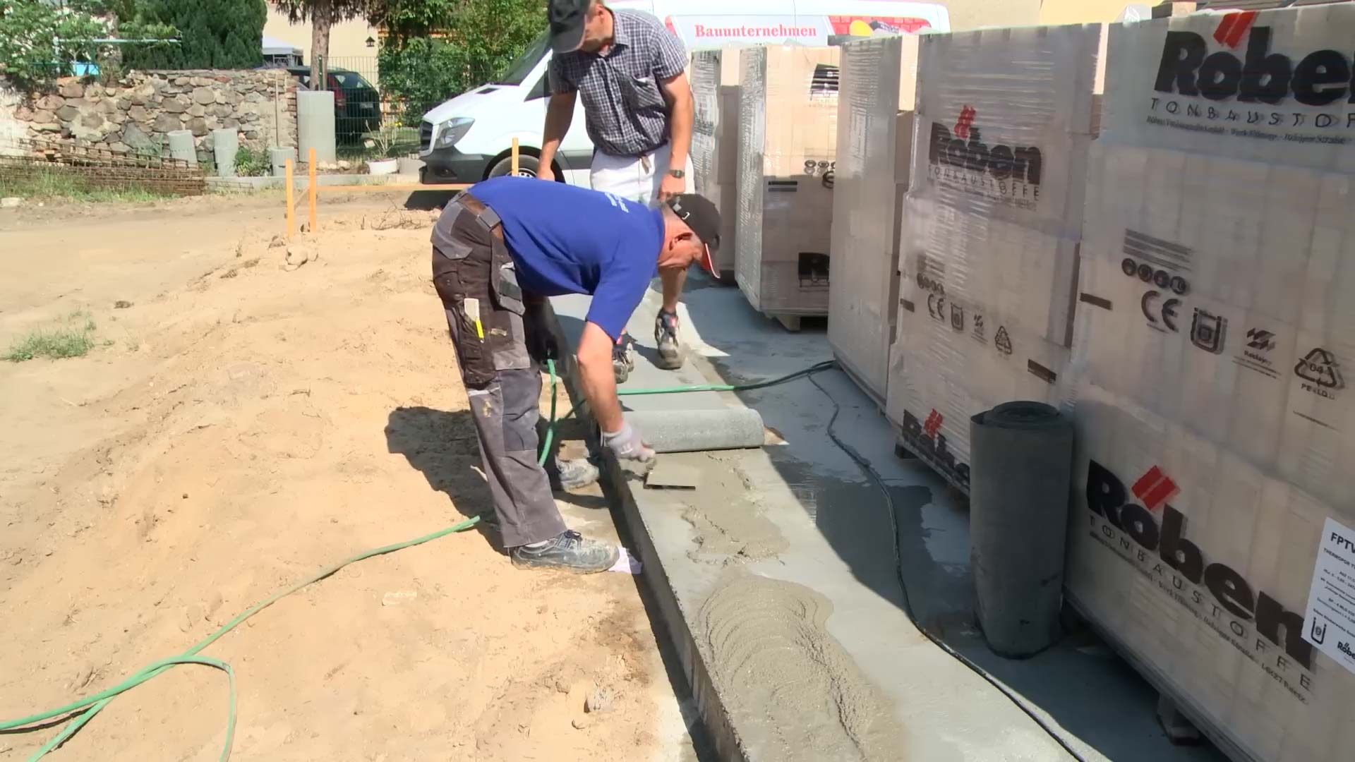 Mauerwerk Hausbau: Ein Bauarbeiter streicht Zementmörtel auf die Bodenplatte eines Hauses