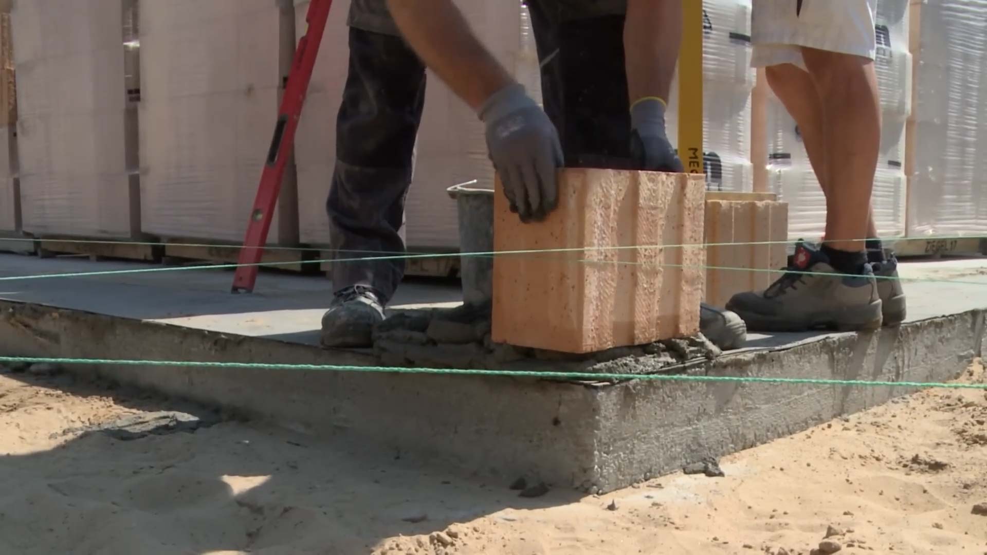 Mauerwerk Hausbau: Ein Maurer verlegt einen roten Ziegelstein in die erste Mauerreihe