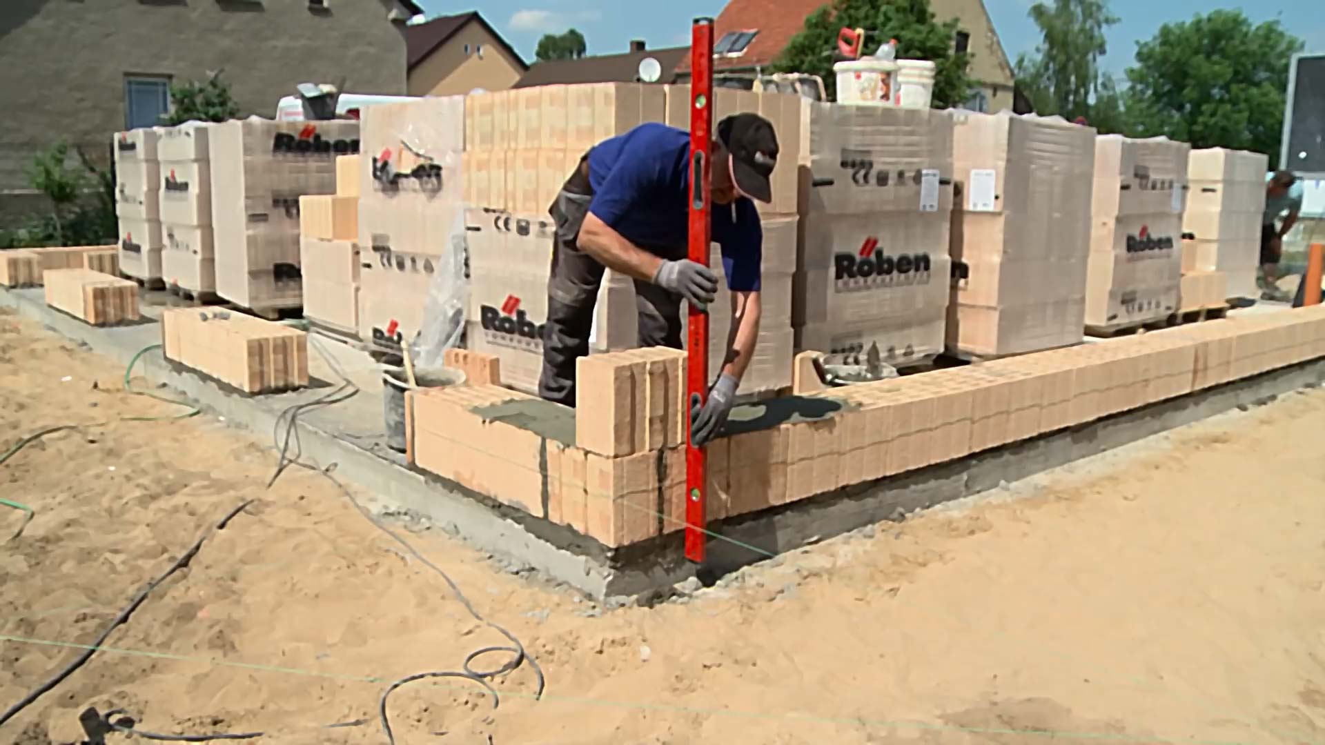 Mauerwerk Hausbau: Ein Maurer misst mithilfe einer Wasserwage, ob die zwei Reihen Ziegelsteine eben liegen