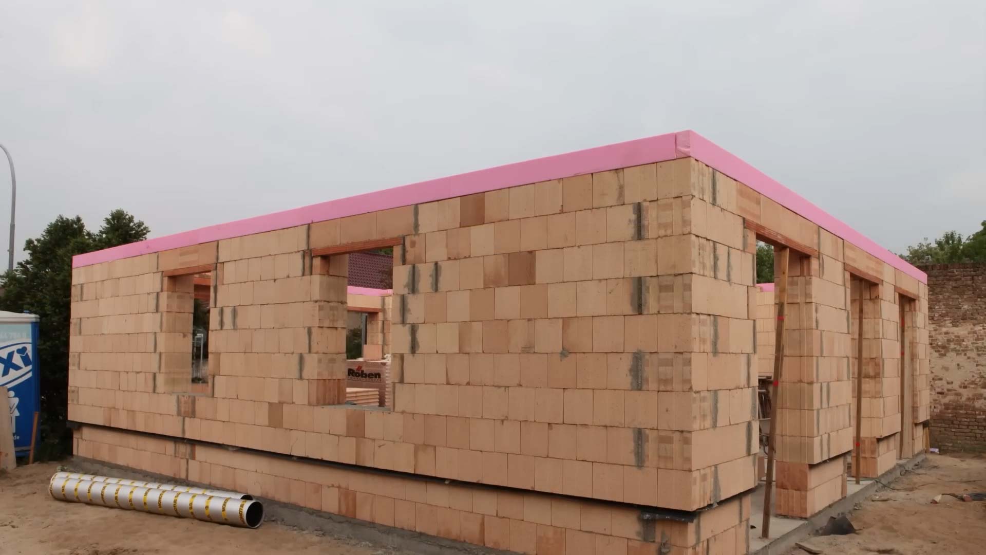 Mauerwerk Hausbau: EIn Haus mit frisch errichteten Mauern aus unverputzten Ziegelsteinen. Oben ist eine rosa Styrodur Schalung zusehen