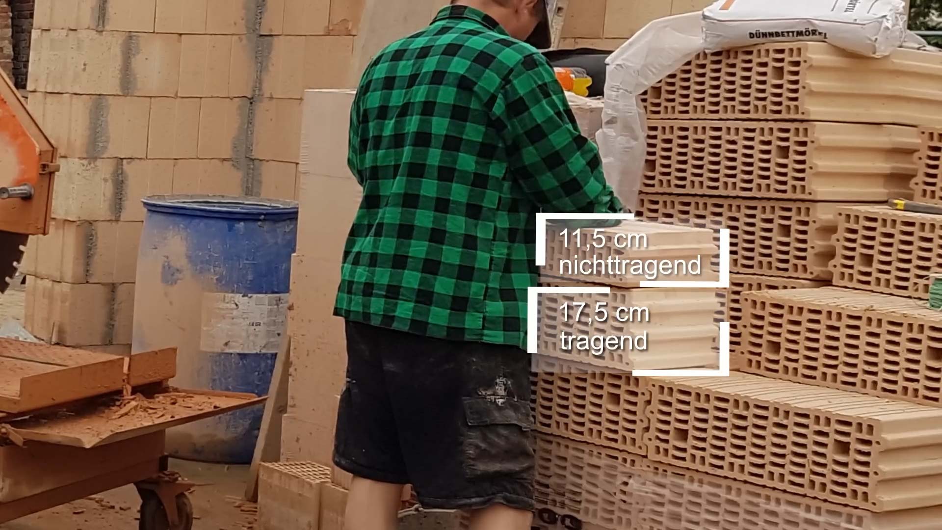 Mauerwerk Hausbau: Ein Mann steht neben einer Palette Zielgelsteine. Auf dem Foto ist markiert, welche Maße ein nicht tragender Zielgestein (11,5 cm) und welche Maße ein tragender Zielgestein (17,5 cm) hat
