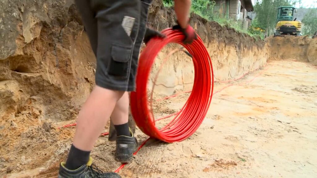 Rohinstallation Sanitär und Heizung: Ein Mann rollt rote Wärmerohre auf dem Boden aus