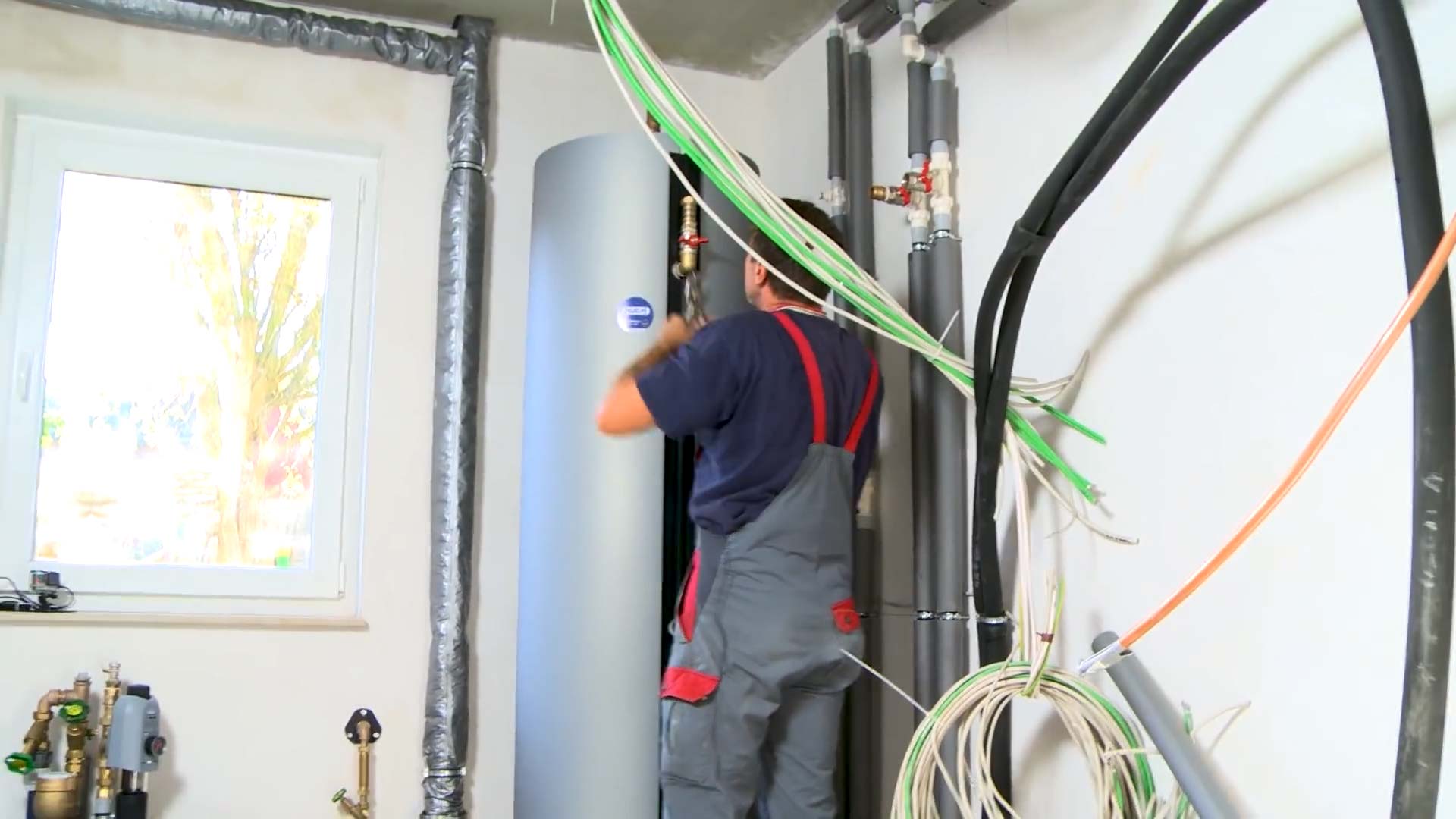 Elektroinstallation Wärmepumpe: Monteur installiert Pufferspeicher und Frischwasserstation.