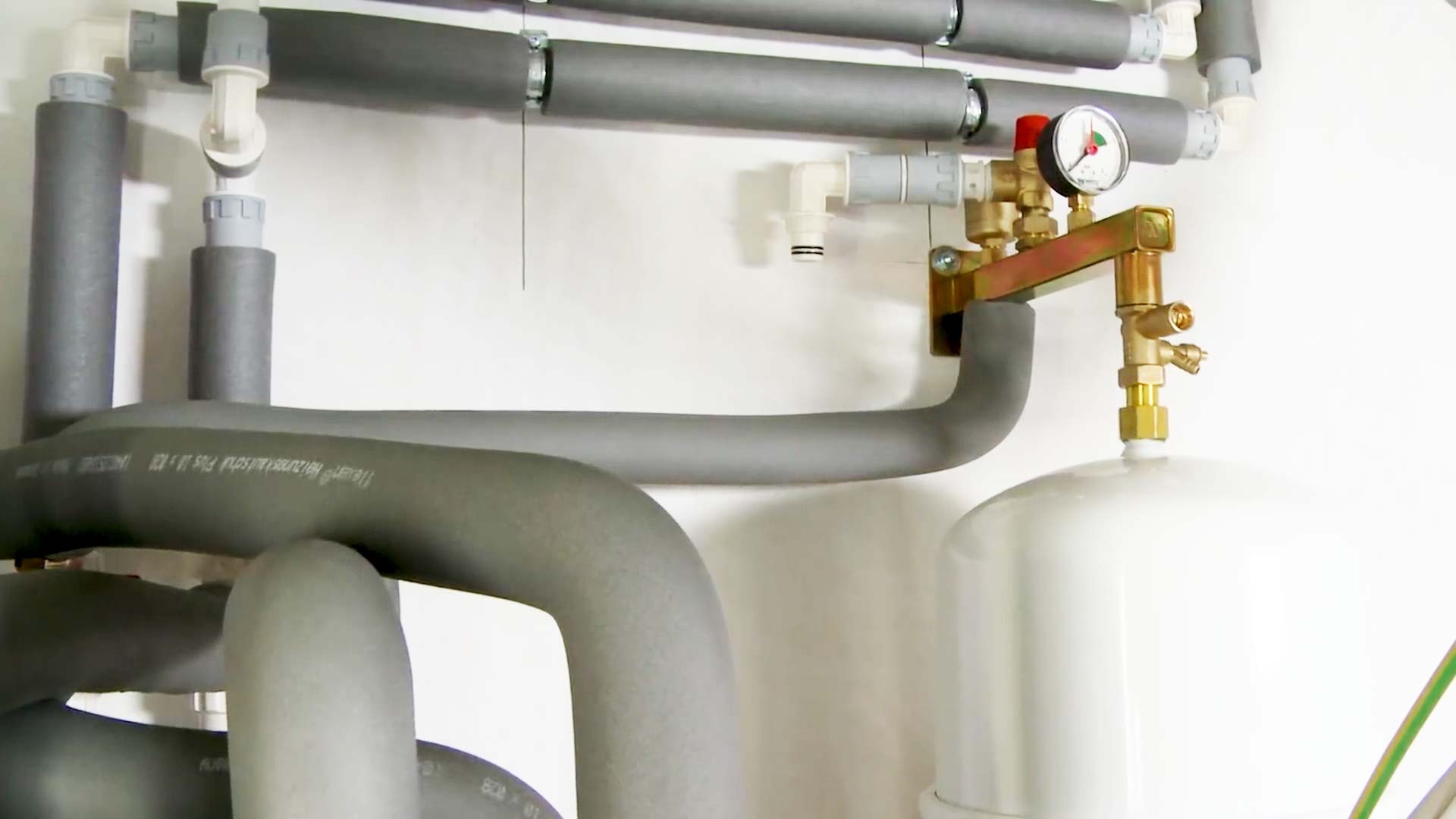 Elektroinstallation Wärmepumpe: Monteur installiert das Sicherheitsventil mit sichtbarer Tropfleitung, verlängert das Abwasserrohr und schließt die Wärmepumpe fachgerecht an die Heizungs- und Erdkollektoranlagen an.