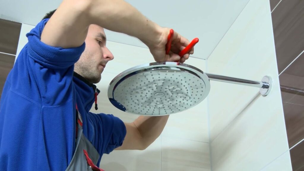 Endmontage Sanitär: Der Monteur bereitet den Anschluss für die Handbrause vor, indem er das Gewinde aufraut und mit Dichtband sowie Silikon versieht. Danach wird die Kopfbrause mit Montagehilfe ausgerichtet und befestigt – die Dusche ist damit komplett montiert.