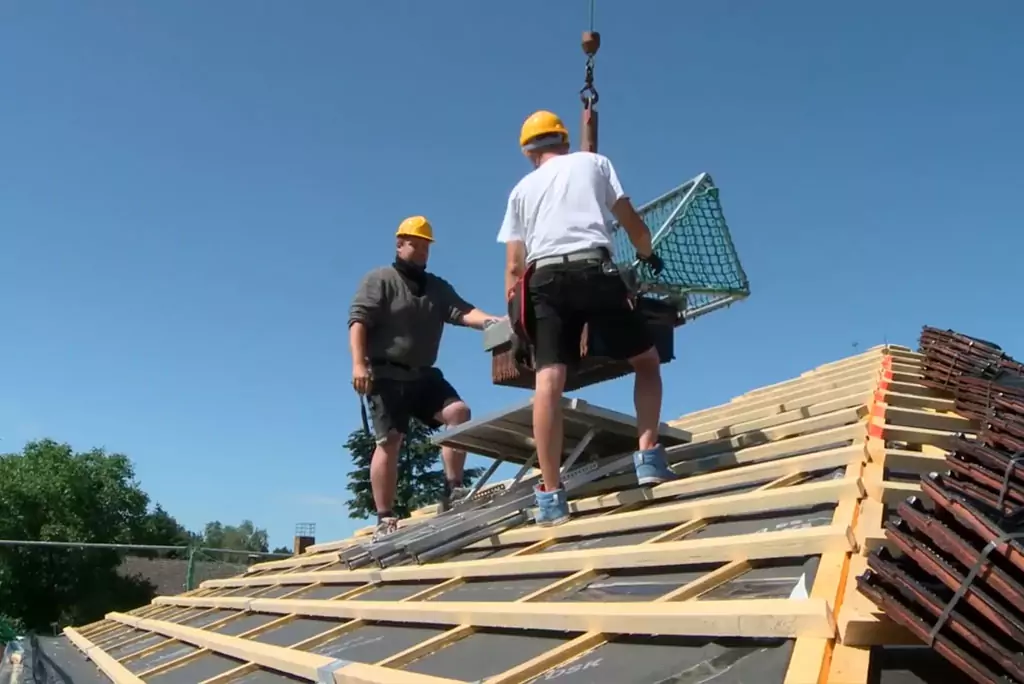 Dachstuhl bauen: Zwei Männer stehen auf einem Dach, welches momentan aus Holzbalken besteht.
